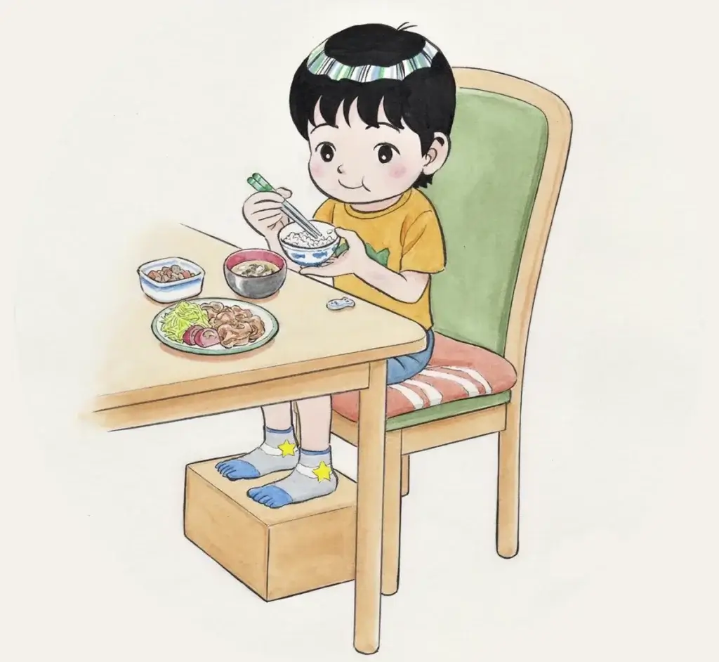 脚を台の上に載せて、安定した状態で食事をする男の子