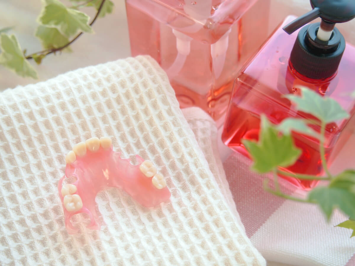 清潔なタオルの上に置かれたピンク色の部分入れ歯と洗浄用品