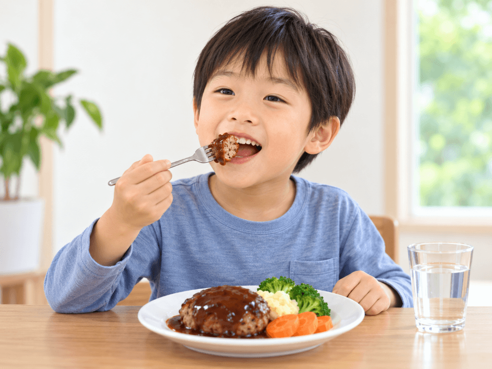歯ごたえのあるおかずをよく噛んで食べる男の子の写真