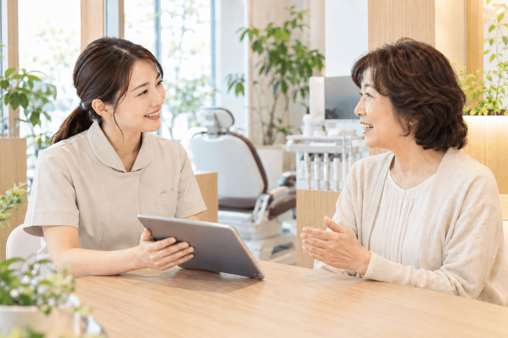歯科医院のスタッフが笑顔で患者さんの話を聞きながら、インプラント治療について相談に応じている様子