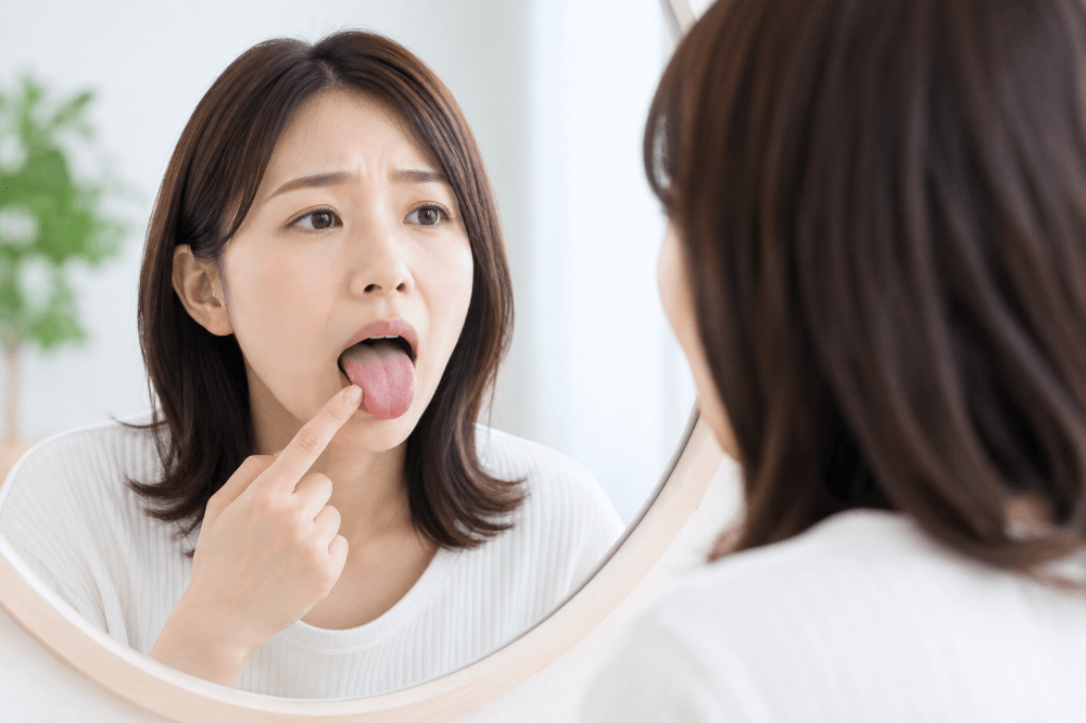 鏡で舌を見ながら口の中の異変をセルフチェックする不安そうな女性の写真