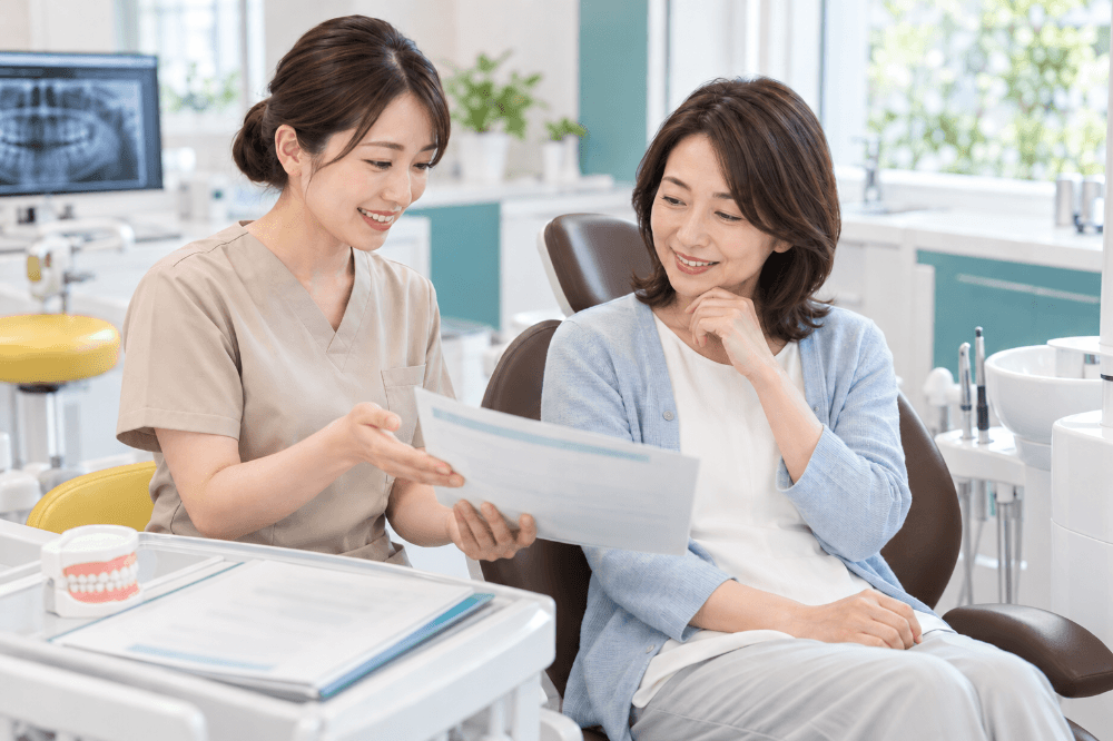 歯科医院のスタッフが患者さんに見積書を見せながら、自費診療の費用を説明している様子
