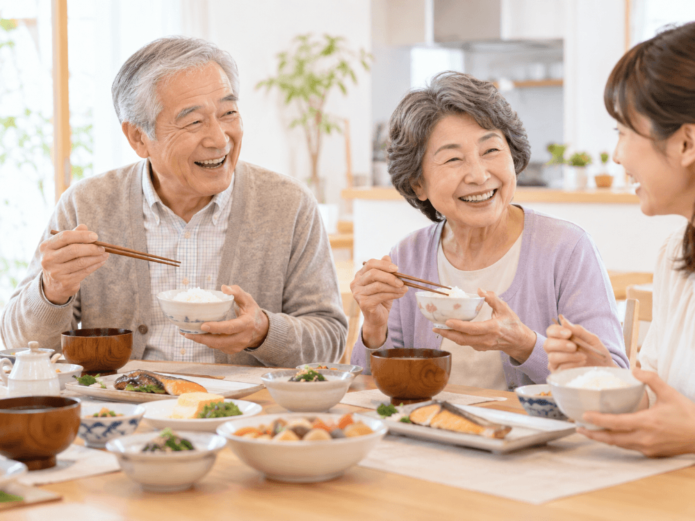 家族と和食の食卓を囲み、ご飯茶碗を手に声を上げて笑い合うシニア夫婦